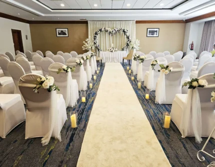 Intimate indoor wedding aisle with white chairs, floral decorations and heart archway