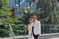 Bride and groom walking together outside a hotel, bride holding sunflowers, leafy terrace (wedding)