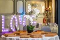 Family enjoying a relaxed hotel celebration with pizzas on a decorated table and illuminated LOVE sign