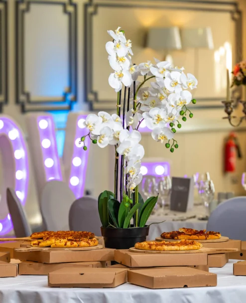 Family enjoying a relaxed hotel celebration with pizzas on a decorated table and illuminated LOVE sign
