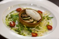 Family enjoying a plated gourmet vegetable tart with salad and cherry tomatoes in a cosy dining setting (no visible text)