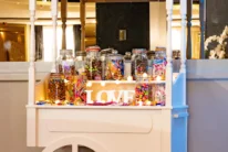 White candy cart with jars of sweets and illuminated "LOVE" sign in a hotel lobby