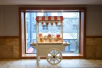 Candy cart with "MR & MRS" bunting and jars of sweets by a hotel window, warm family treat display