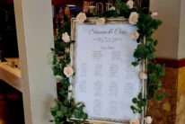 Wedding seating chart on a floral‑framed easel with roses and greenery in hotel foyer