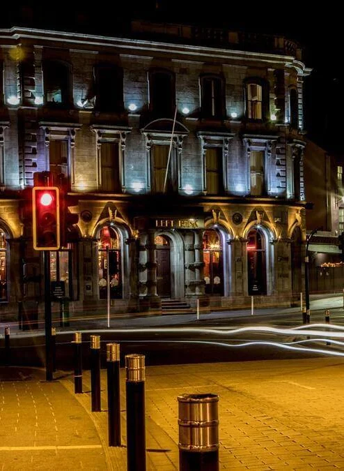 Evening street outside a warm, illuminated hotel/pub with a family strolling nearby and light trails