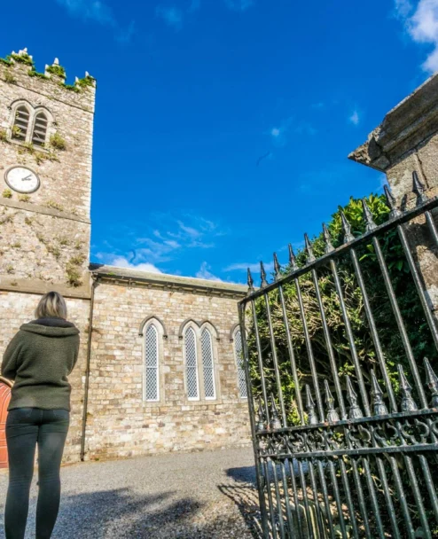 Family exploring a historic stone church courtyard under a bright blue sky, iron gate visible