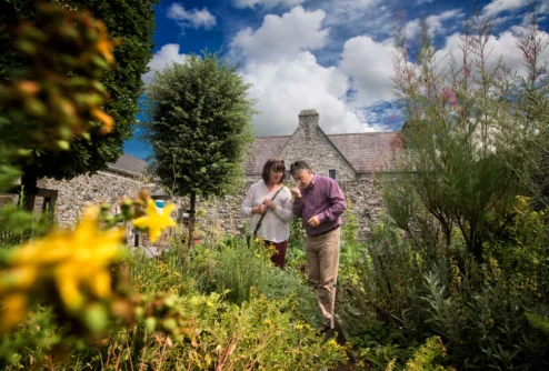 Mature couple smelling herbs together in a sunny cottage garden with stone walls and blue sky