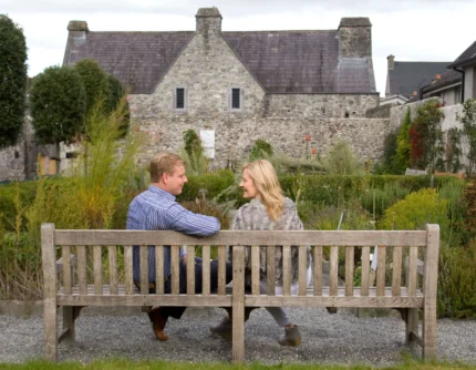 Couple seated on a wooden bench in a walled garden, smiling and enjoying a peaceful hotel courtyard view