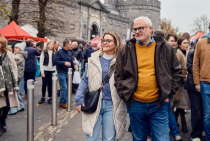 Middle-aged couple strolling through an outdoor market by a historic castle, smiling together