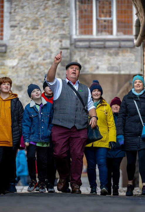 Family group on a guided walk through a stone alley, smiling and spotting sights together (no visible text)