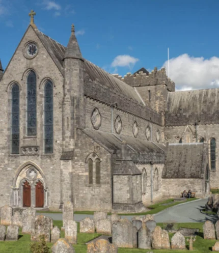 Family strolling near an ancient stone cathedral and round tower with graveyard under blue sky