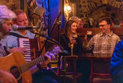 Family enjoying pints and live music in cosy stone-walled pub, couple smiling and toasting (no visible text)