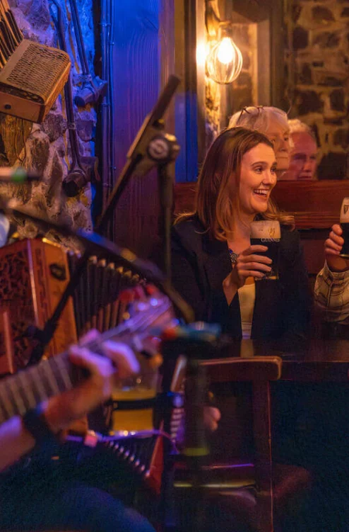 Family enjoying pints and live music in cosy stone-walled pub, couple smiling and toasting (no visible text)