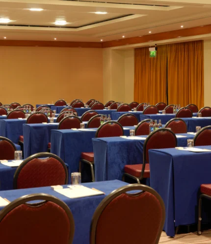 Conference room set for a family or group retreat, rows of tables with notepads, water and projector screen