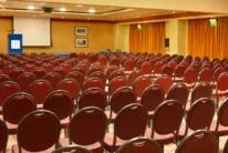 Rows of red chairs set for a family conference in a warm hotel meeting room with podium and screen