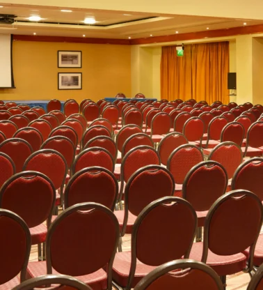 Rows of red chairs set for a family conference in a warm hotel meeting room with podium and screen