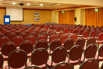 Rows of red chairs set for a family conference in a warm hotel meeting room with podium and screen