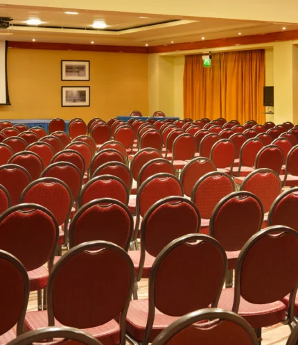 Rows of red chairs set for a family conference in a warm hotel meeting room with podium and screen