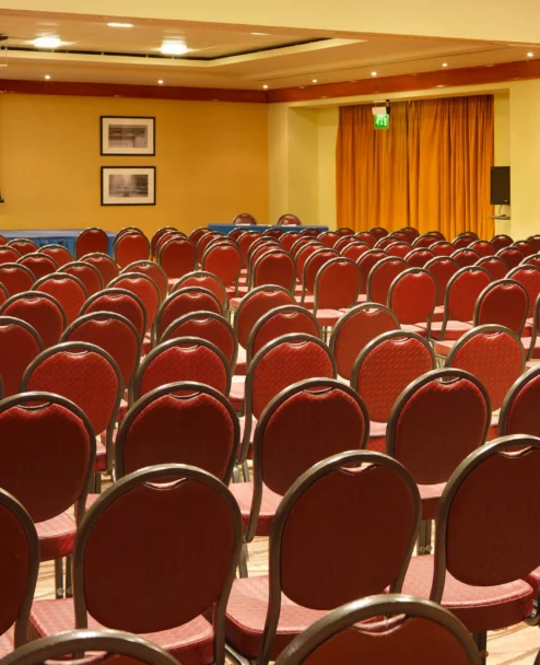 Rows of red chairs set for a family conference in a warm hotel meeting room with podium and screen