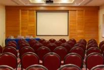 Empty hotel conference room with rows of red chairs facing a projector screen, warm wood walls, ready for a family event or meeting