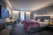 Family-friendly hotel bedroom with king bed, cosy seating, welcome TV screen text, and flowers