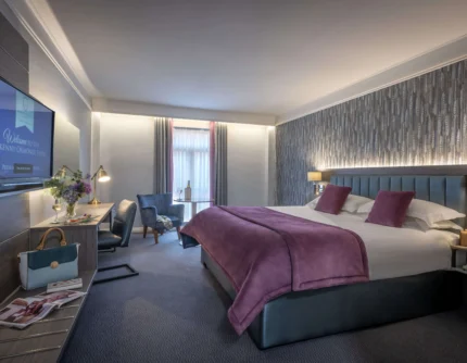 Family-friendly hotel bedroom with king bed, cosy seating, welcome TV screen text, and flowers