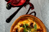 Warm family dining: savoury mini tart with melted cheese and greens, poached plums in red sauce on a grey plate