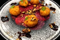 Crispy golden croquette bites on beet carpaccio with walnut pieces and berry compote, plated elegantly