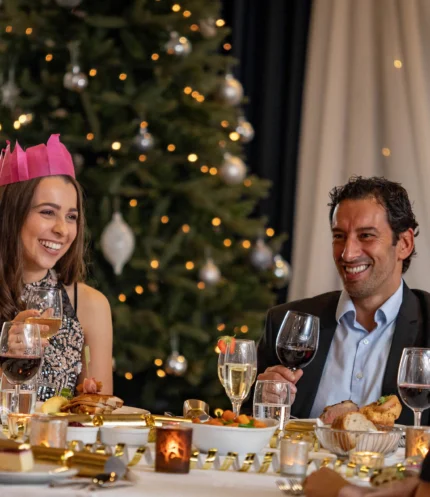 Family group enjoying a festive hotel dinner by a decorated Christmas tree, laughing and toasting