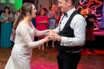 Newlywed couple dancing joyfully at a hotel wedding reception with applauding family nearby