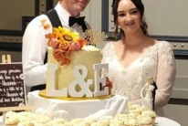 Newlywed couple standing behind a personalised wedding cake and cupcakes at reception