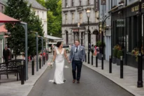 Newlywed couple strolling hand in hand down a charming town street, bride with bouquet