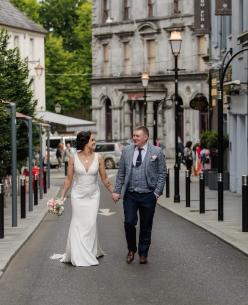 Newlywed couple strolling hand in hand down a charming town street, bride with bouquet