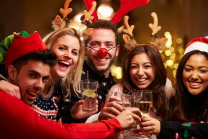 Family group in festive jumpers and antler headbands cheers with drinks in a warmly lit hotel lounge