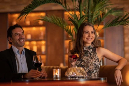 Smiling couple enjoying cocktails in a warm hotel bar lounge with soft candlelight and plants