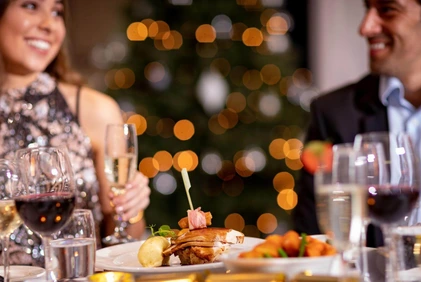 Smiling couple toast with wine at a festive hotel dinner table, warm bokeh lights